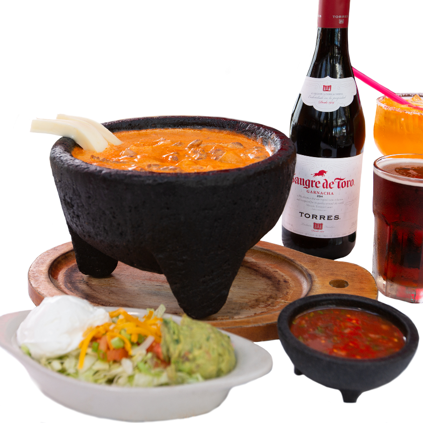 Close-up of Molcajete dish served in a traditional stone bowl, accompanied by Sangre de Toro wine, salsa, and side dishes.